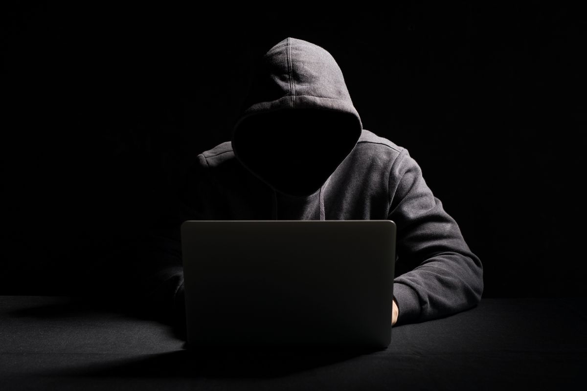 Unrecognizable hacker on laptop in the dark